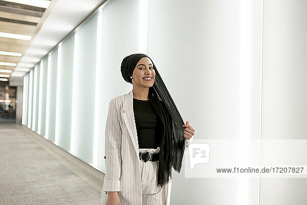 Glückliche arabische Frau  die beim Einkaufen im Einkaufszentrum an der Wand steht
