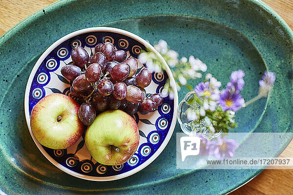 Schale mit frischen reifen Trauben und Äpfeln mit Blume