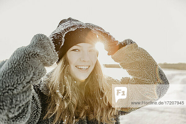 Portrait of beautiful teenage girl adjusting knit hat while smiling at camera