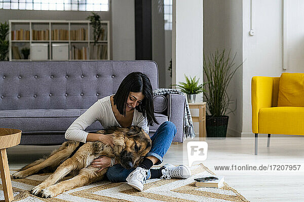Cheerful woman embracing dog while sitting on carpet in living room