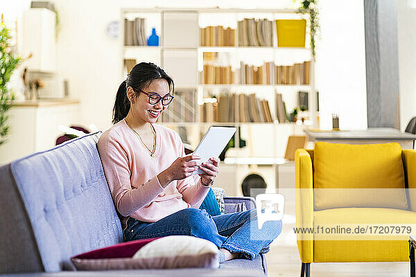 Lächelnde junge Frau  die zu Hause ein digitales Tablet benutzt