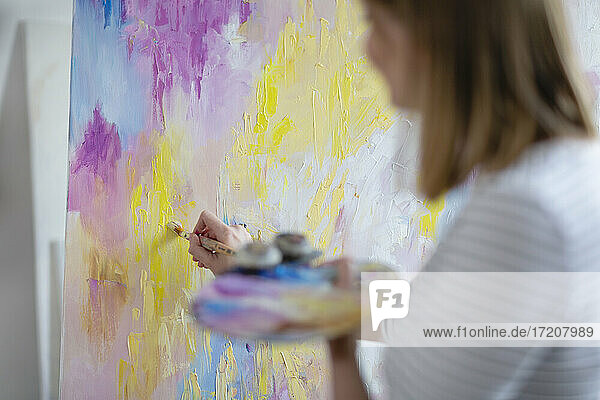 Mid adult woman painting abstract canvas at home studio