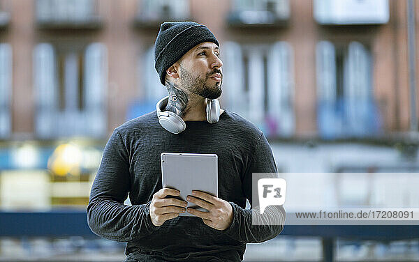 Hipster-Mann mit Kopfhörern  der ein digitales Tablet hält und wegschaut