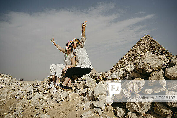 Ägypten  Kairo  Zwei Touristinnen sitzen zusammen auf einem Felsen mit der Großen Pyramide von Gizeh im Hintergrund