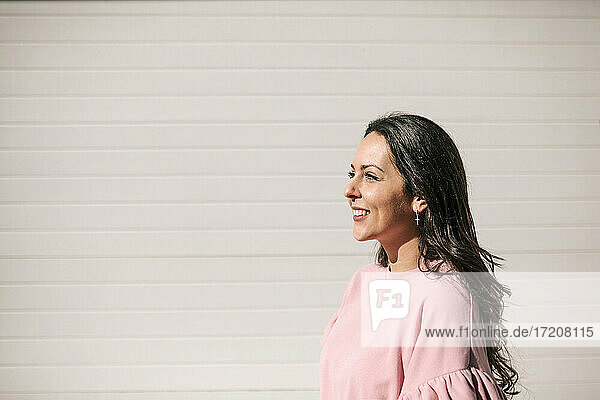 Lächelnde Frau an einer Mauer stehend an einem sonnigen Tag