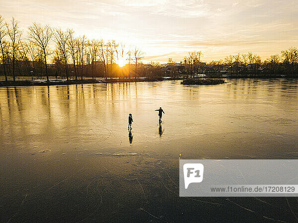 Freunde beim Schlittschuhlaufen auf einem zugefrorenen Teich bei Sonnenuntergang