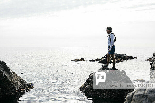 Mann  der die Aussicht betrachtet  während er auf einer Felsformation im Wasser gegen den klaren Himmel steht