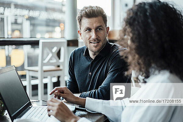 Businessman discussing with colleague using laptop while sitting at cafe