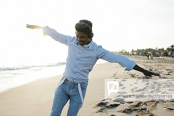 Happy Afro man doing airplane pose at beach during sunny day
