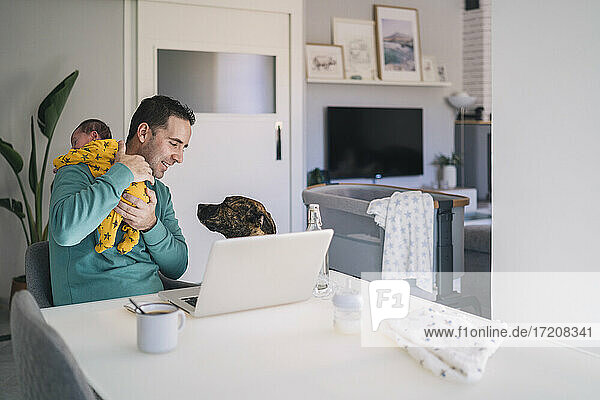 Father carrying son while looking at dog in home office