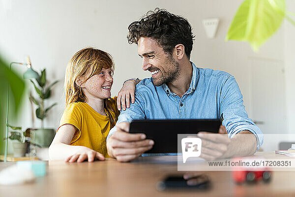 Vater mit digitalem Tablet  der seine Tochter anlächelt  während er zu Hause sitzt