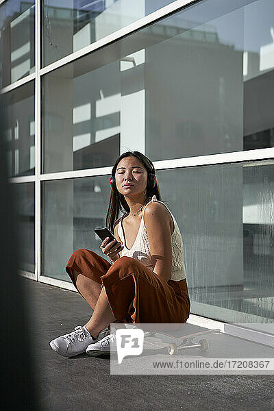 Junge Frau mit Smartphone hört Musik über Kopfhörer an einem sonnigen Tag