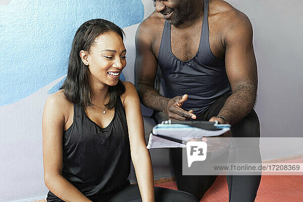 Smiling young woman looking at digital tablet held by fitness instructor
