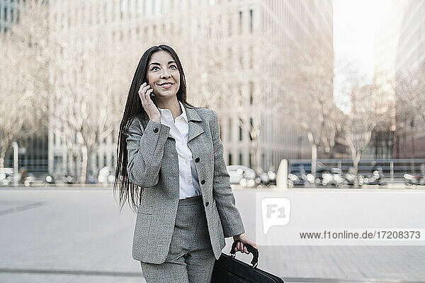 Lächelnde Geschäftsfrau  die in der Stadt mit einem Smartphone telefoniert