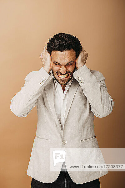 Angry businessman with head in hands standing against brown background