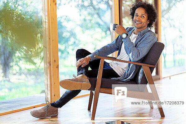 Lächelnder Mann mit Kaffeetasse auf einem Sessel im Vorgarten sitzend