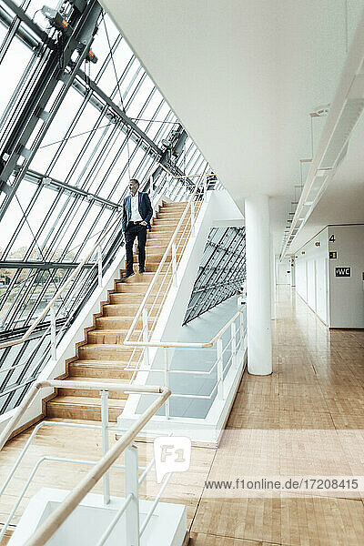 Geschäftsmann  der durch ein Fenster schaut  während er von einer Treppe im Bürokorridor nach unten geht