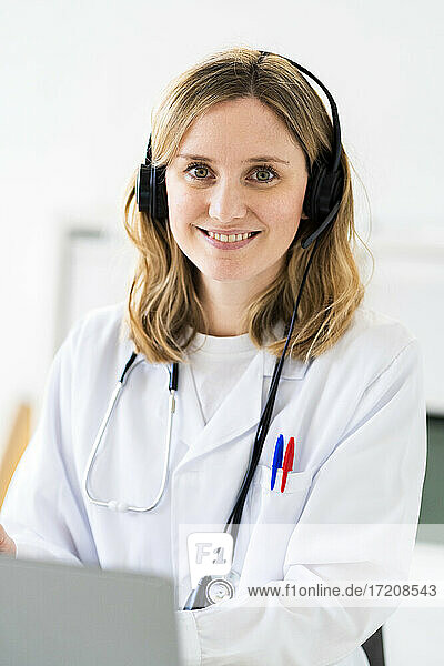 Smiling female medical professional wearing headphones during online consultation at medical clinic