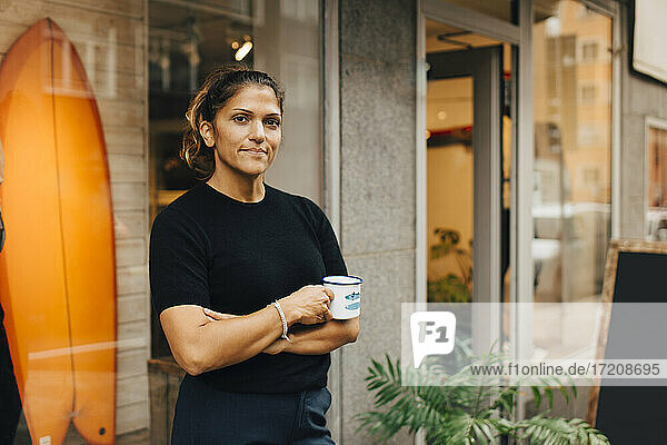 Porträt einer Besitzerin mit Kaffeetasse vor einem Bekleidungsgeschäft