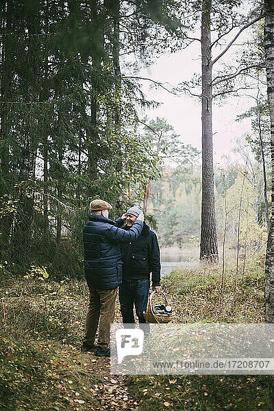 Homosexual couple with picnic basket standing in forest