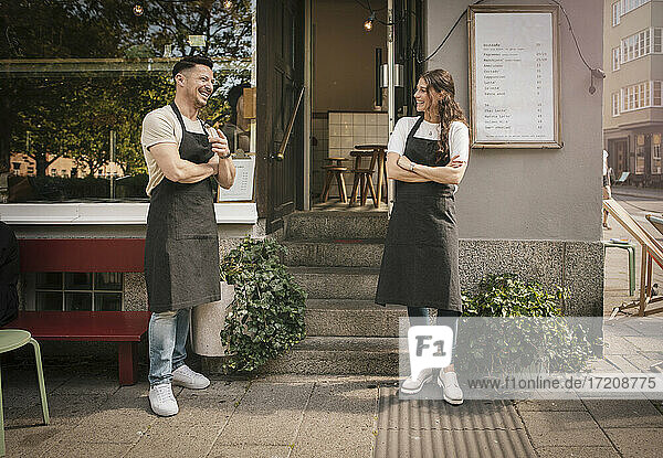 Lächelnde weibliche und männliche Café-Besitzer stehen vor einem Delikatessengeschäft