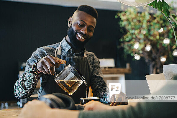 Smiling male owner pouring tea in cup at coffee shop