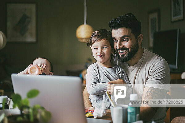 Lächelnder Sohn und Vater  die während der Pandemie zu Hause Online-Ratschläge über den Laptop einholen