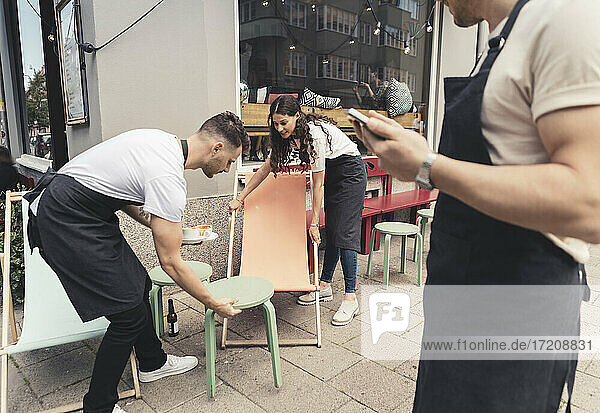 Männliche und weibliche Unternehmer arrangieren Tische und Stühle vor dem Cafe