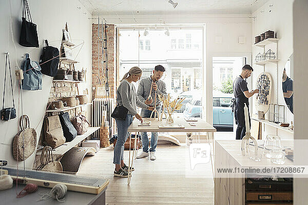 Clients looking at jewelry while male owner working in design studio