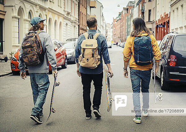 Rear view of male friends with skateboards walking in city