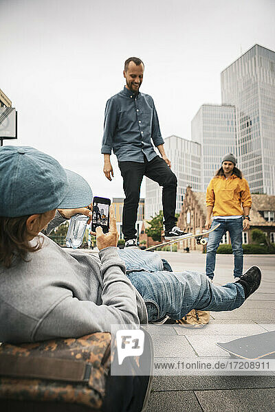 Mann fotografiert  während männlicher Freund auf Fußweg skatet