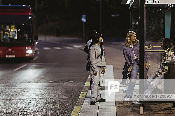 Female friends sitting on bus stop at night