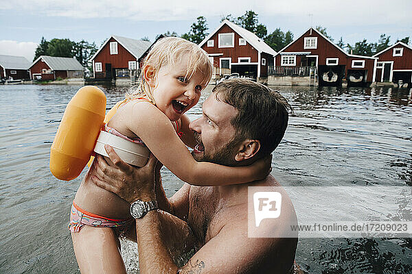 Portrait of cheerful daughter with father in lake during vacations