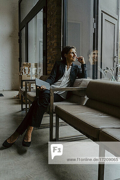 Lächelnde Geschäftsfrau schaut durch  während sie im Büro sitzt