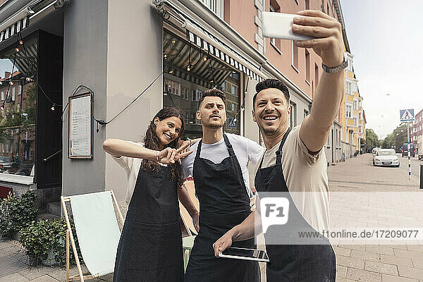 Lächelnde männliche und weibliche Besitzer  die Selfie auf Smartphone außerhalb Cafe