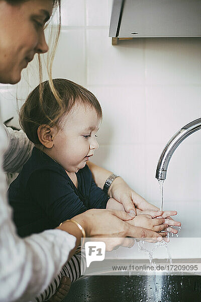 Mutter hilft Baby Mädchen Hände waschen unter Waschbecken in der Küche