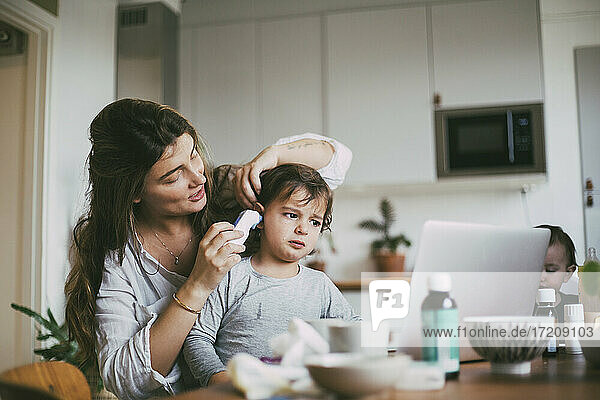 Mother checking son's ear through otoscope at home