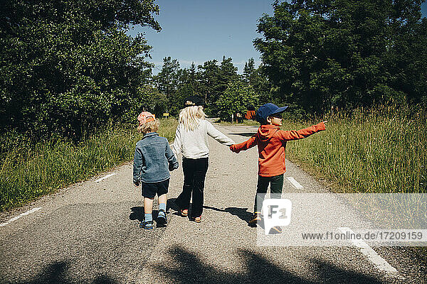 Rear view of sister with brothers walking on road during sunny day