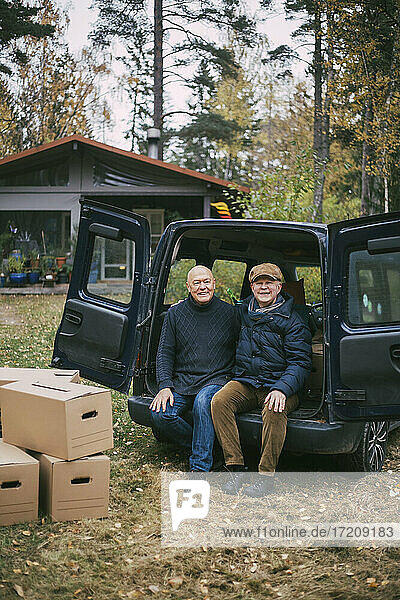 Porträt eines lächelnden homosexuellen Paares  das im Kofferraum eines Autos im Hinterhof sitzt