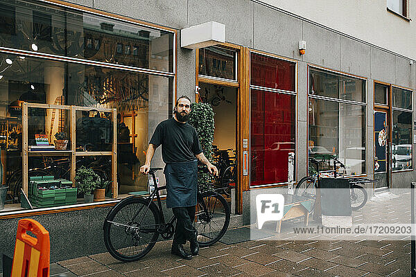 Bärtiger männlicher Besitzer steht vor der Werkstatt am Fahrrad