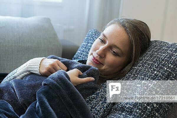 Eine junge Frau liegt in eine Decke eingekuschelt auf einem Sofa in Dorfen  Bayern  Deutschland  Europa