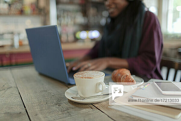 Frau arbeitet am Laptop neben Cappuccino und Croissant im Café