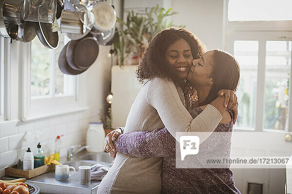 Mutter und Tochter umarmen und küssen in der Küche