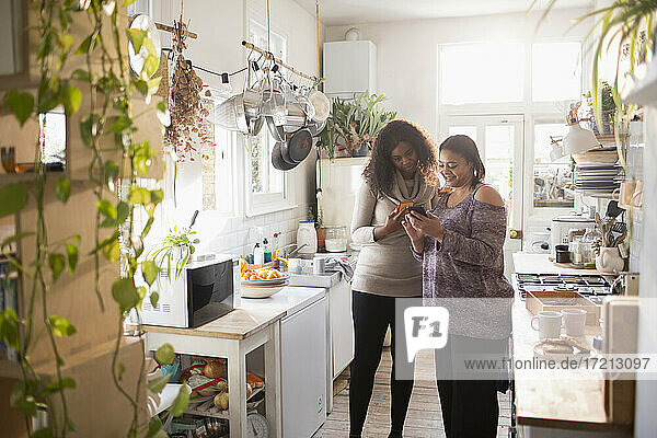 Mother and daughter using smart phone in kitchen