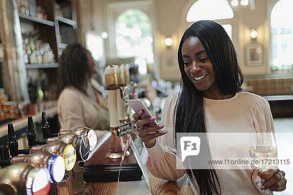 Glückliche junge Frau mit Smartphone und trinken Weißwein im Pub