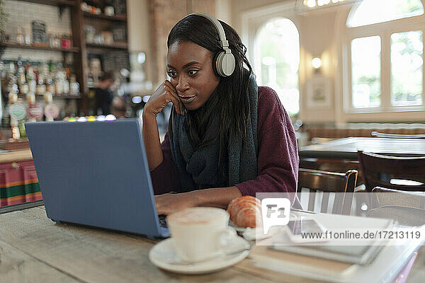 Young businesswoman with headphones working at laptop in cafe