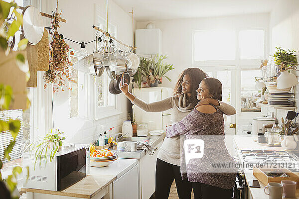 Glückliche Mutter und Tochter nehmen selfie in sonnigen Küche