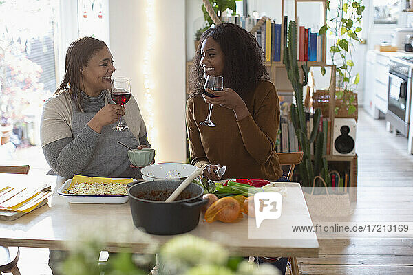 Mutter und Tochter kochen und trinken Rotwein am Tisch