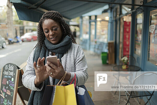 Frau mit Smartphone und Einkaufstüten auf dem Gehweg