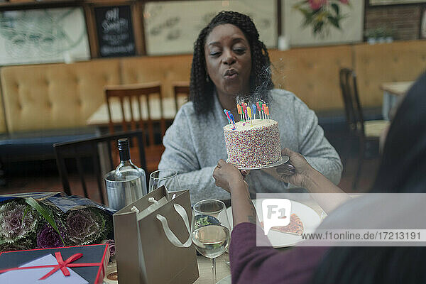 Mutter Ausblasen Geburtstagskerze auf Kuchen im Restaurant mit Tochter
